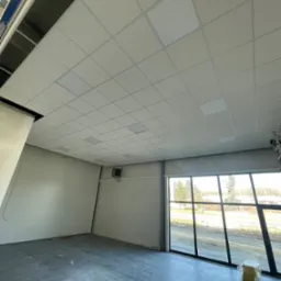 Montaż sufitu kasetonowego w pomieszczeniu biurowym z dużymi oknami, widoczne niedokończone fragmenty i elementy konstrukcyjne.