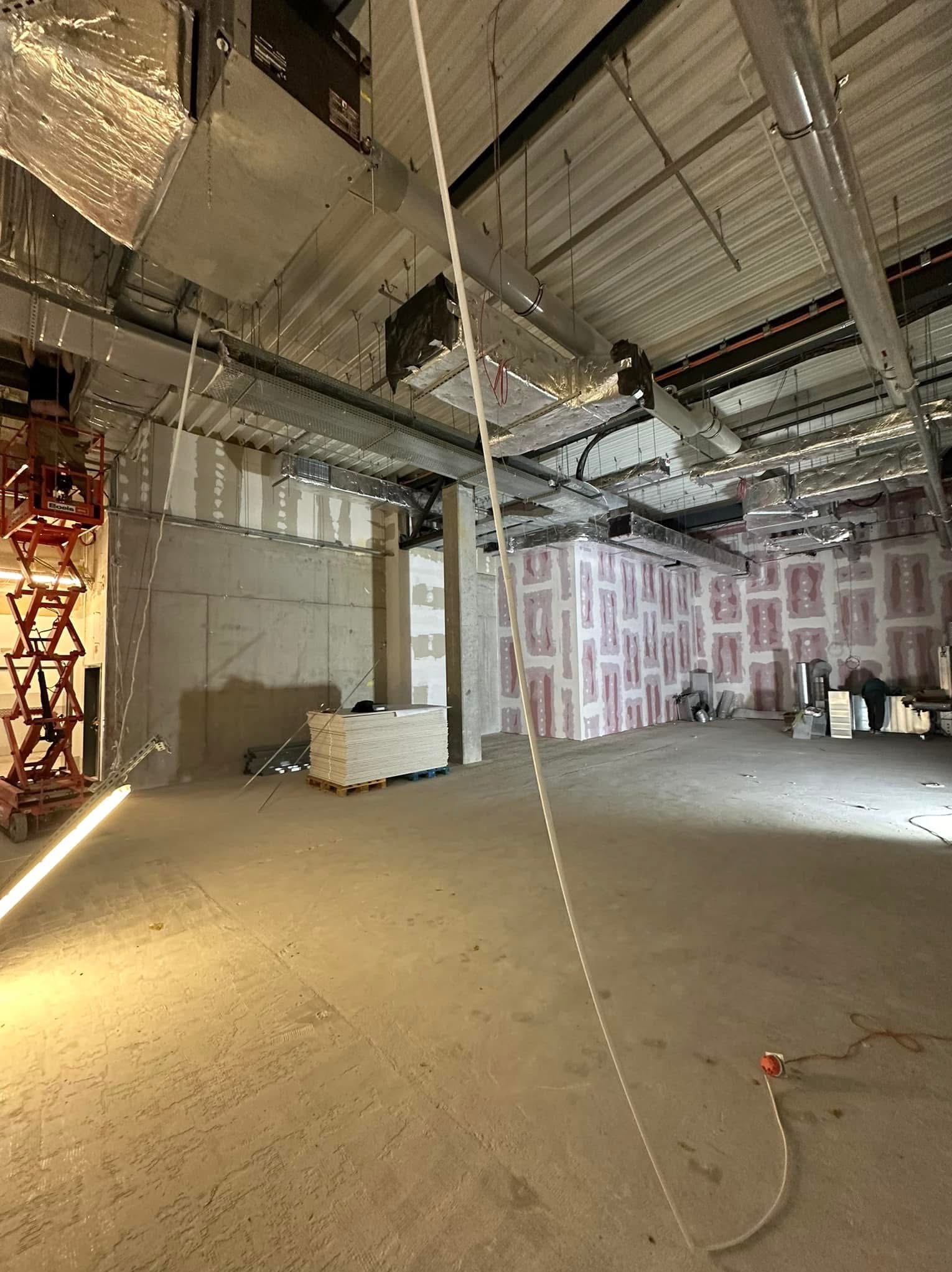 Wnętrze w trakcie remontu: widoczna konstrukcja sufitu, izolacja ścian, paleta płyt i podnośnik nożycowy.
