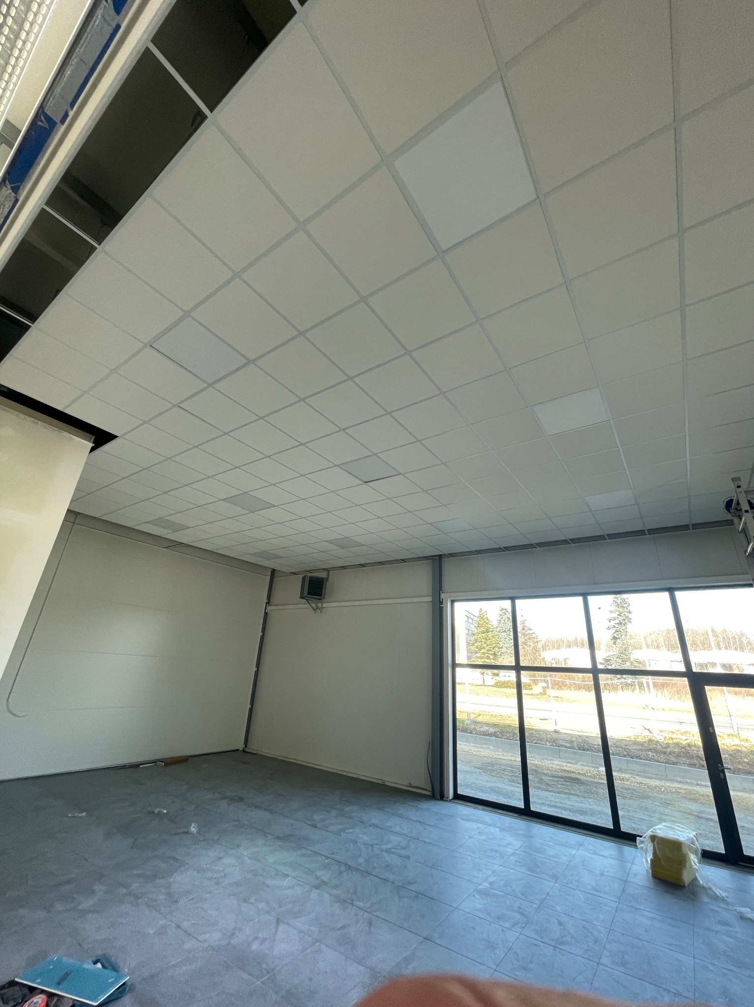 Montaż sufitu kasetonowego w pomieszczeniu biurowym z dużymi oknami, widoczne niedokończone fragmenty i elementy konstrukcyjne.