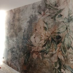 Wymarzony Dom ArtEmi - Ściana z fototapetą o motywie kwiatowym w odcieniach brązu i zieleni, zabezpieczona folią podłoga, widoczne gniazdka elektryczne.