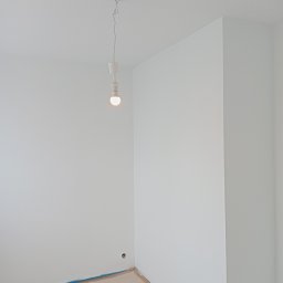 Wymarzony Dom ArtEmi - Pomalowane na biało ściany w rogu pokoju, zabezpieczona podłoga, wisząca żarówka bez klosza.