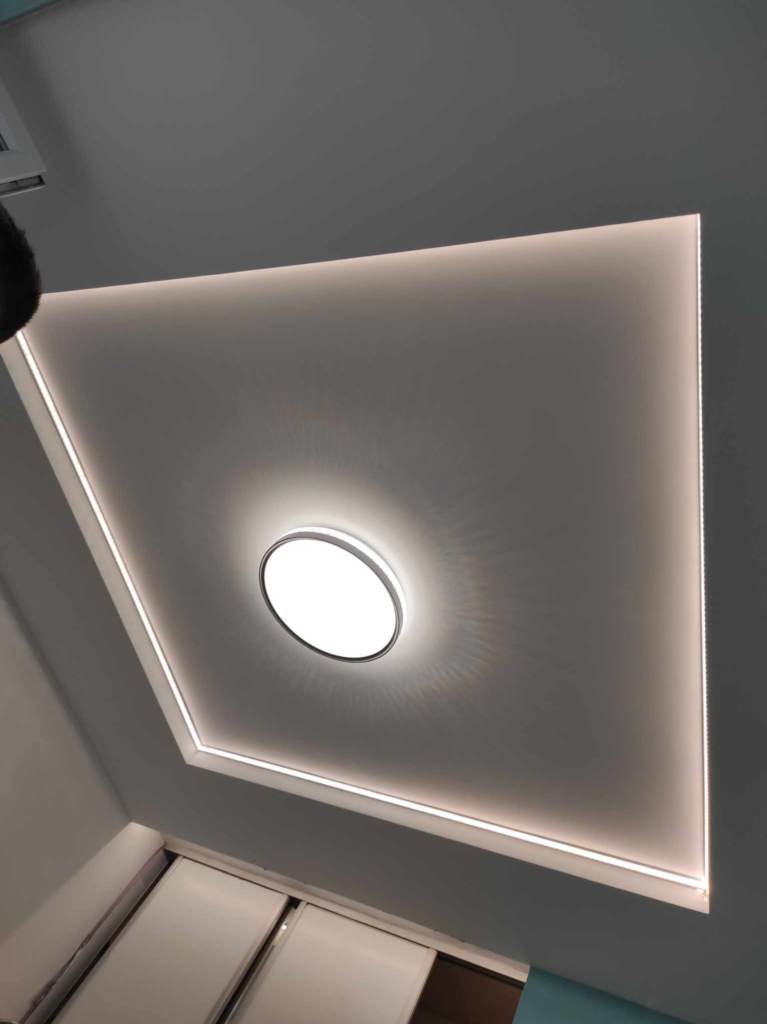 Biały sufit z oświetleniem LED w kształcie kwadratu i okrągłą lampą centralną, widok z dołu.