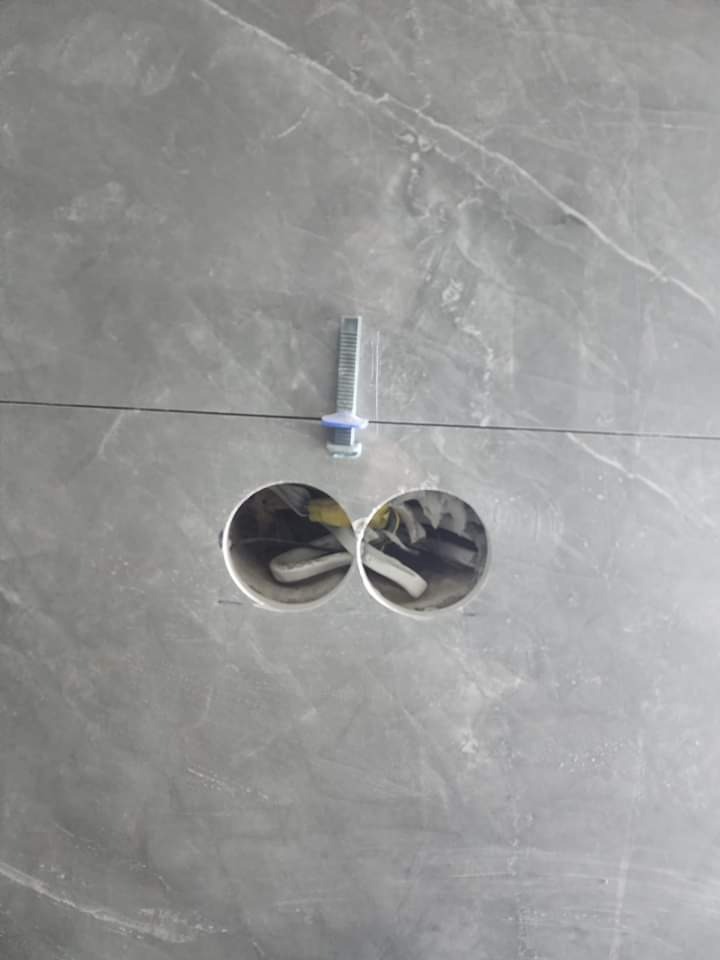 Szara marmurowa ściana z dwoma wywierconymi otworami, w których widoczne są przewody, oraz poziomica przymocowana do ściany.