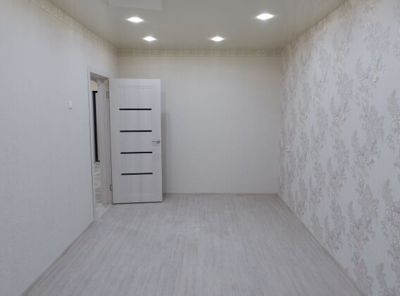 Pusty pokój po remoncie z białą, nowoczesną stolarką drzwiową z czarnymi poziomymi wstawkami i wzorzystą tapetą na jednej ze ścian, oświetlony przez wpuszczane lampy sufitowe.