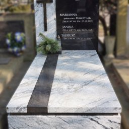 Kamieniarstwo GRANBUD Waldemar Rycyk - Granitowy pomnik z czarną tablicą nagrobną i białym krzyżem, udekorowany gałązką świerku i zniczem, na tle cmentarza.