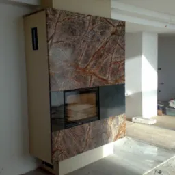 Nowoczesny, obudowany w brązowy marmur z wyraźnym żyłkowaniem, kominek z czarnym wkładem, w surowym wnętrzu w trakcie prac wykończeniowych.