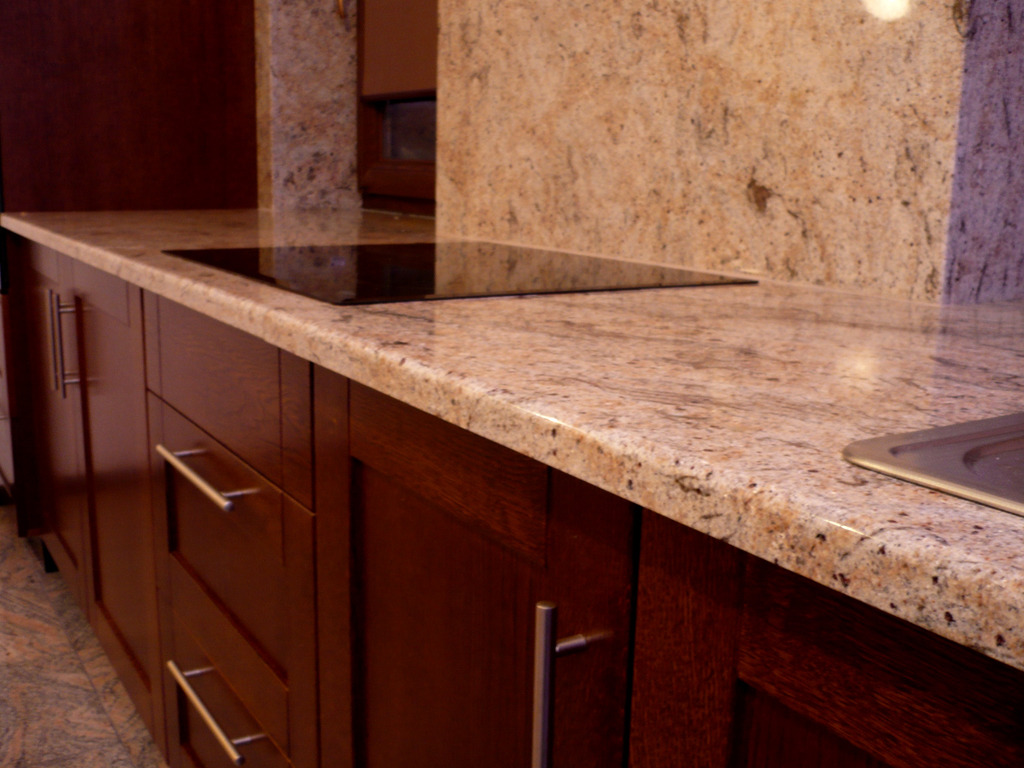 Jasny, nakrapiany blat z kamienia w kuchni z ciemnymi, drewnianymi szafkami i wbudowaną płytą grzewczą.