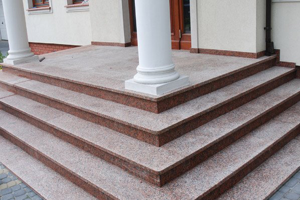 Zewnętrzne schody wejściowe z czerwono-szarego granitu, prowadzące do budynku z kolumnami, widoczne z dołu.