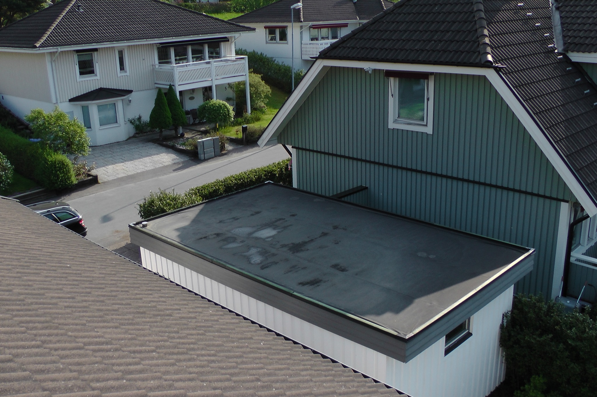 Widok z góry na płaski dach pokryty papą, z widocznymi śladami po wodzie i innymi budynkami w tle.