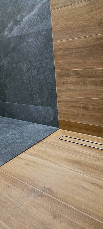 Nowoczesna łazienka z szarymi płytkami imitującymi kamień i drewnopodobnymi panelami, z odpływem liniowym. Minimalistyczny design, eleganckie wykończenie.