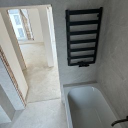 Sergio - Wykończona łazienka w szarościach z wanną i czarnym grzejnikiem drabinkowym, widok na remontowane pomieszczenie obok.