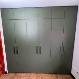 Meble, kuchnie, szafy, stoliki na wymiar. - Duża, oliwkowa szafa wnękowa z metalowymi uchwytami, dopasowana do sufitu, na podłodze z płytek imitujących drewno.