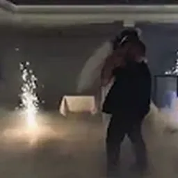 Para młoda tańczy w dymie, z fontanną iskier po lewej stronie. Ujęcie z wesela, słabe oświetlenie, para w ciemnych strojach, biały welon panny młodej.