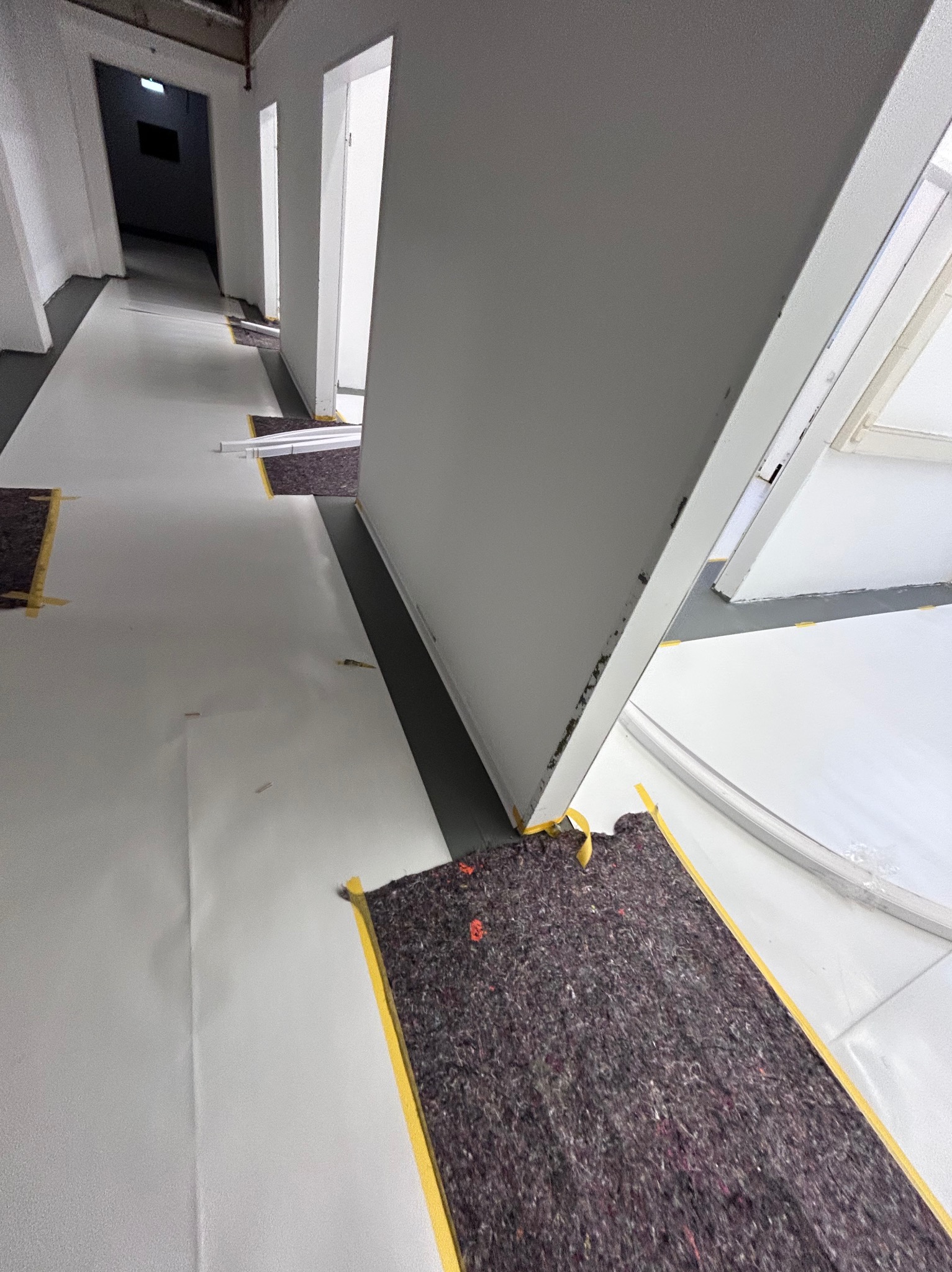 Przygotowanie do malowania biura w Bydgoszczy: podłoga zabezpieczona folią i matą, ściany gruntowane. Widoczne detale wykończeniowe i taśmy malarskie.