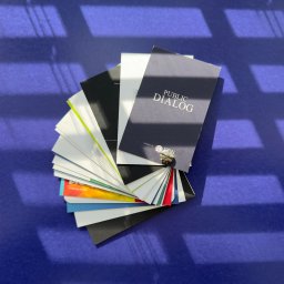 TM DRUK IWONA CIANCIARA - Kaskada różnorodnych, gotowych wizytówek z napisem 'PUBLIC DIALOG' na wierzchu, ułożonych wachlarzowo na fioletowym tle z cieniem okiennym.