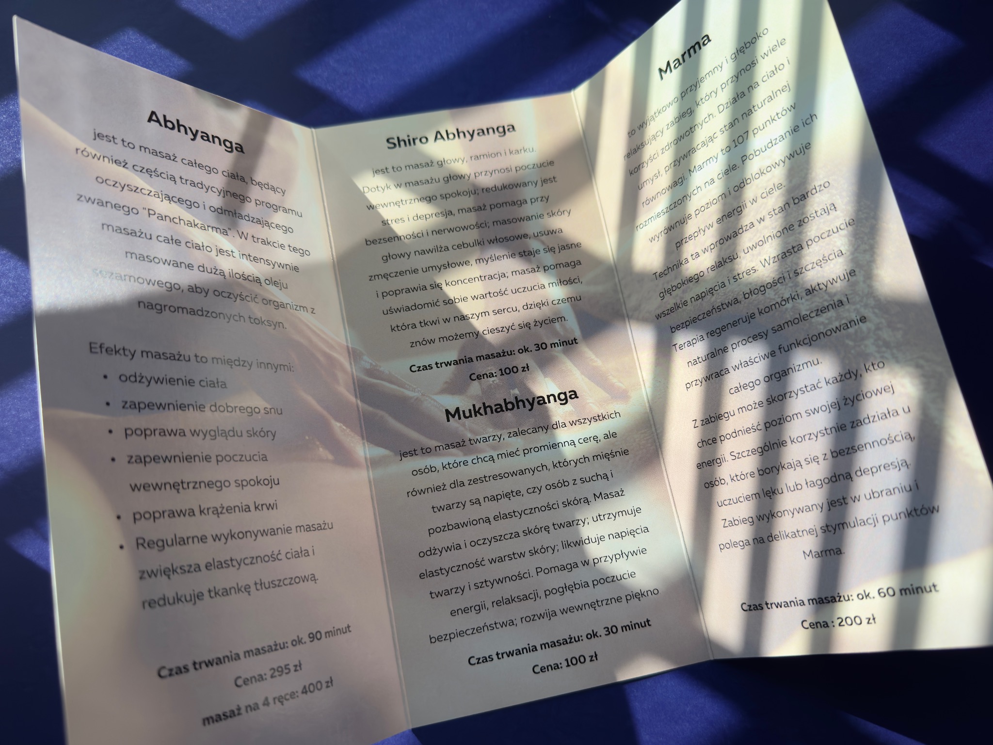 Ulotka składana prezentująca ofertę masaży Abhyanga, Shiro Abhyanga, Mukhabhyanga i Marma w Warszawie, z podanymi czasami trwania i cenami.