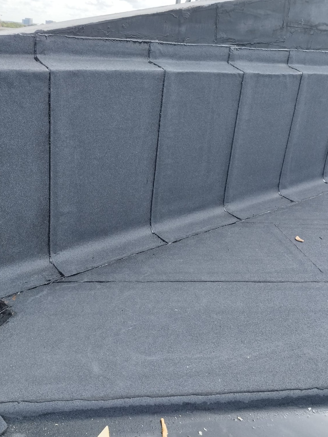 Szczegółowe ujęcie płaskiego dachu pokrytego papą termozgrzewalną z widocznymi łączeniami i obróbkami blacharskimi przy attyce.