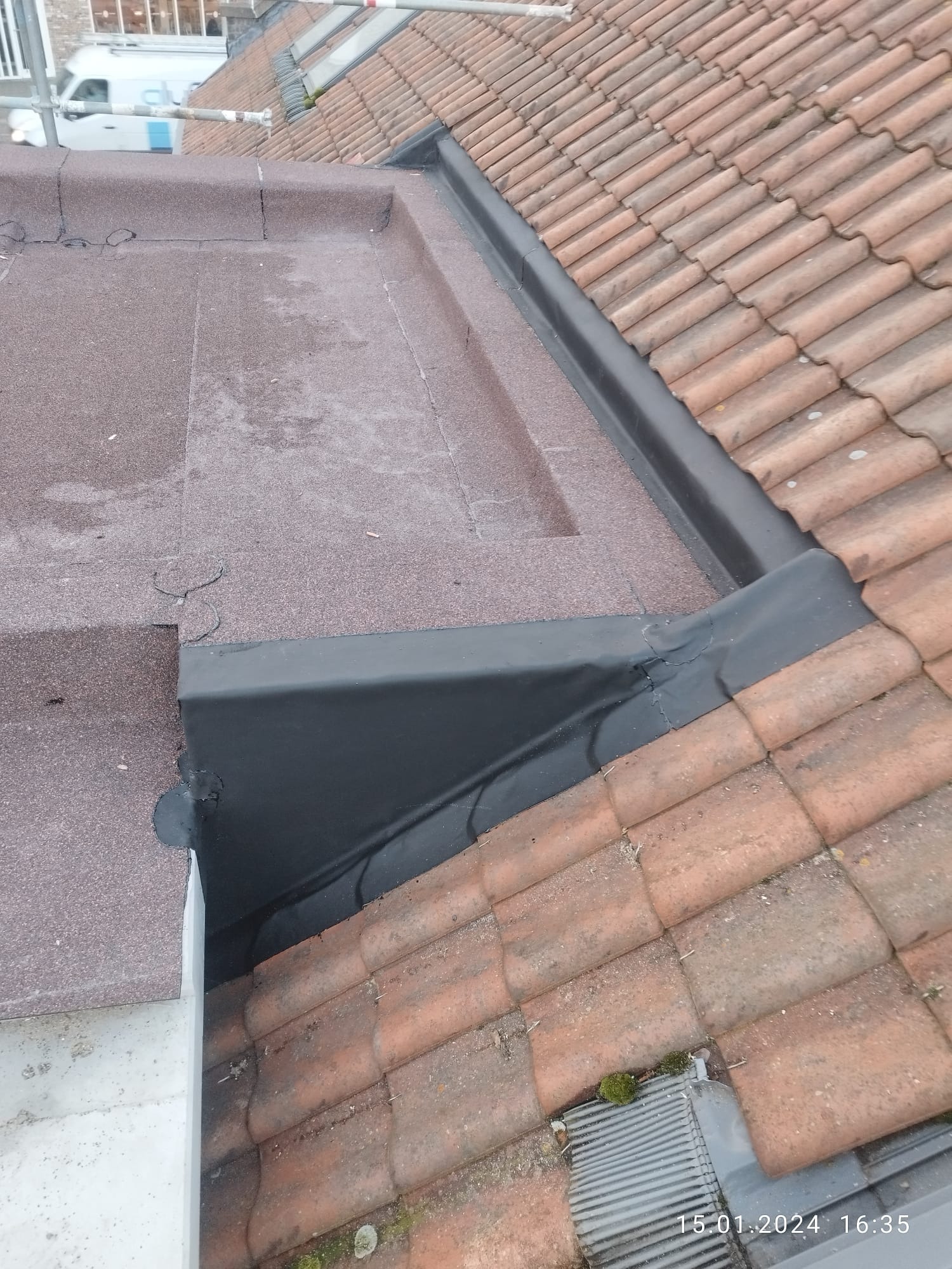 Połączenie dachu płaskiego pokrytego papą z dachem skośnym z dachówki ceramicznej, z widocznymi obróbkami blacharskimi w kolorze czarnym.