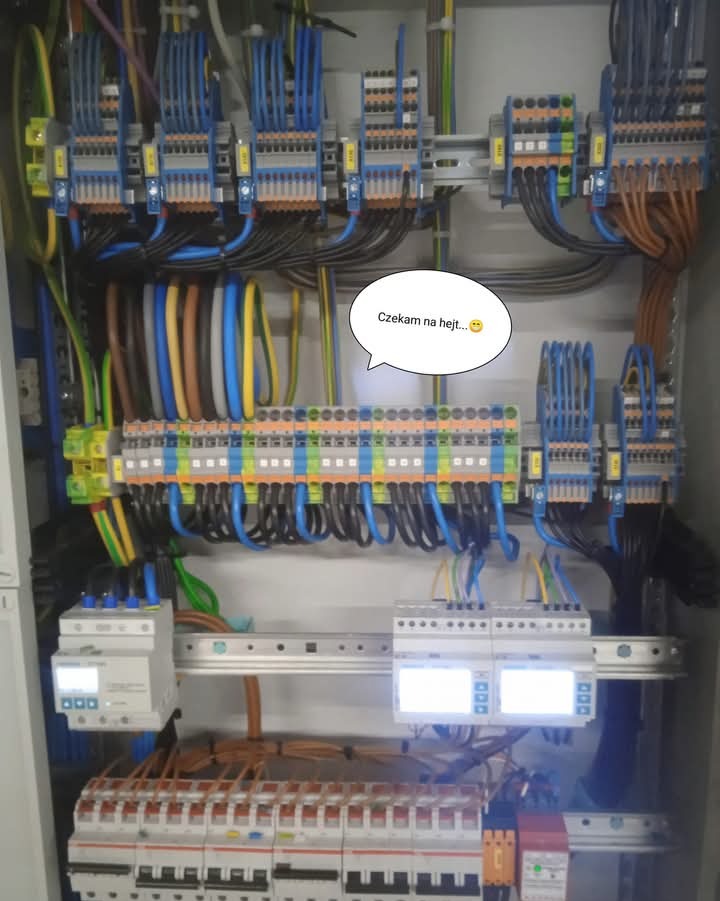 Rozdzielnia elektryczna z widocznymi zabezpieczeniami, listwami zaciskowymi i uporządkowanym okablowaniem, z naklejką 'Czekam na hejt...' w dymku.