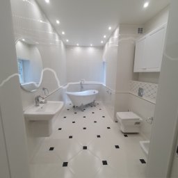 WP-BUD - Elegancka łazienka w bieli z czarnymi akcentami na podłodze. Wolnostojąca wanna na ozdobnych nóżkach, umywalka na postumencie i okrągłe lustro. Minimalistyczny design.