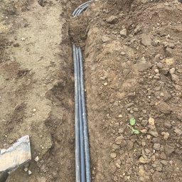 NOIBUD - Wkopane rury w ziemi, prawdopodobnie system nawadniania. Widoczny fragment łopaty. Ujęcie z góry, ziemia z kamieniami.