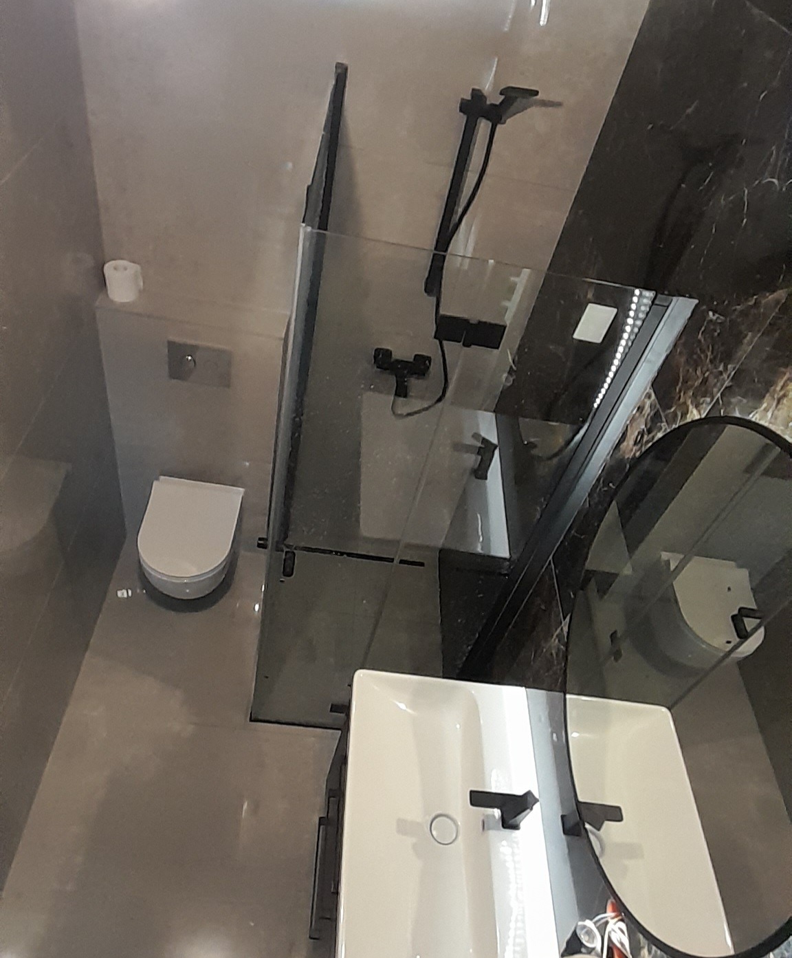 Nowoczesna łazienka z kabiną prysznicową typu walk-in z czarnymi detalami, wiszącą miską WC i umywalką nablatową, widok z góry.