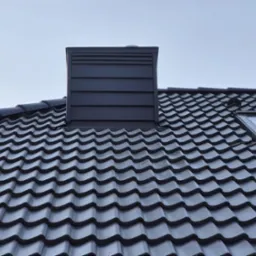 Ciemna dachówka ceramiczna na dachu domu z oknem dachowym i kominem wykończonym blachą w kolorze dachu.