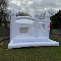 Biały dmuchany zamek z dwiema różowymi balonami na trawie w Jaworznie, ustawiony na tle pochmurnego nieba.