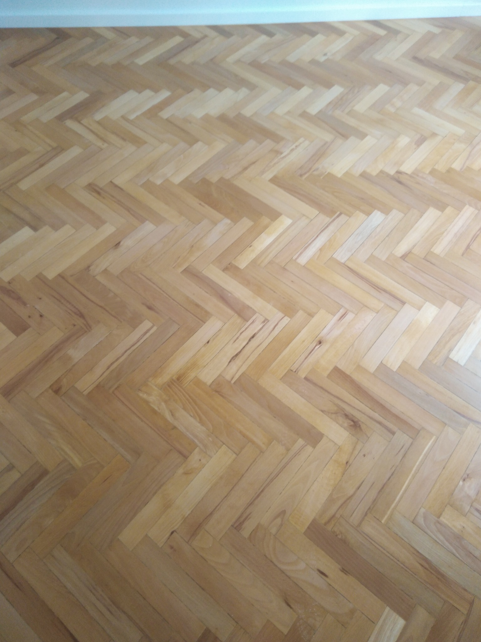 Parkiet ułożony w jodełkę z jasnego drewna, widok z góry. Naturalne odcienie drewna i wzór jodełki tworzą klasyczny i elegancki wygląd podłogi.