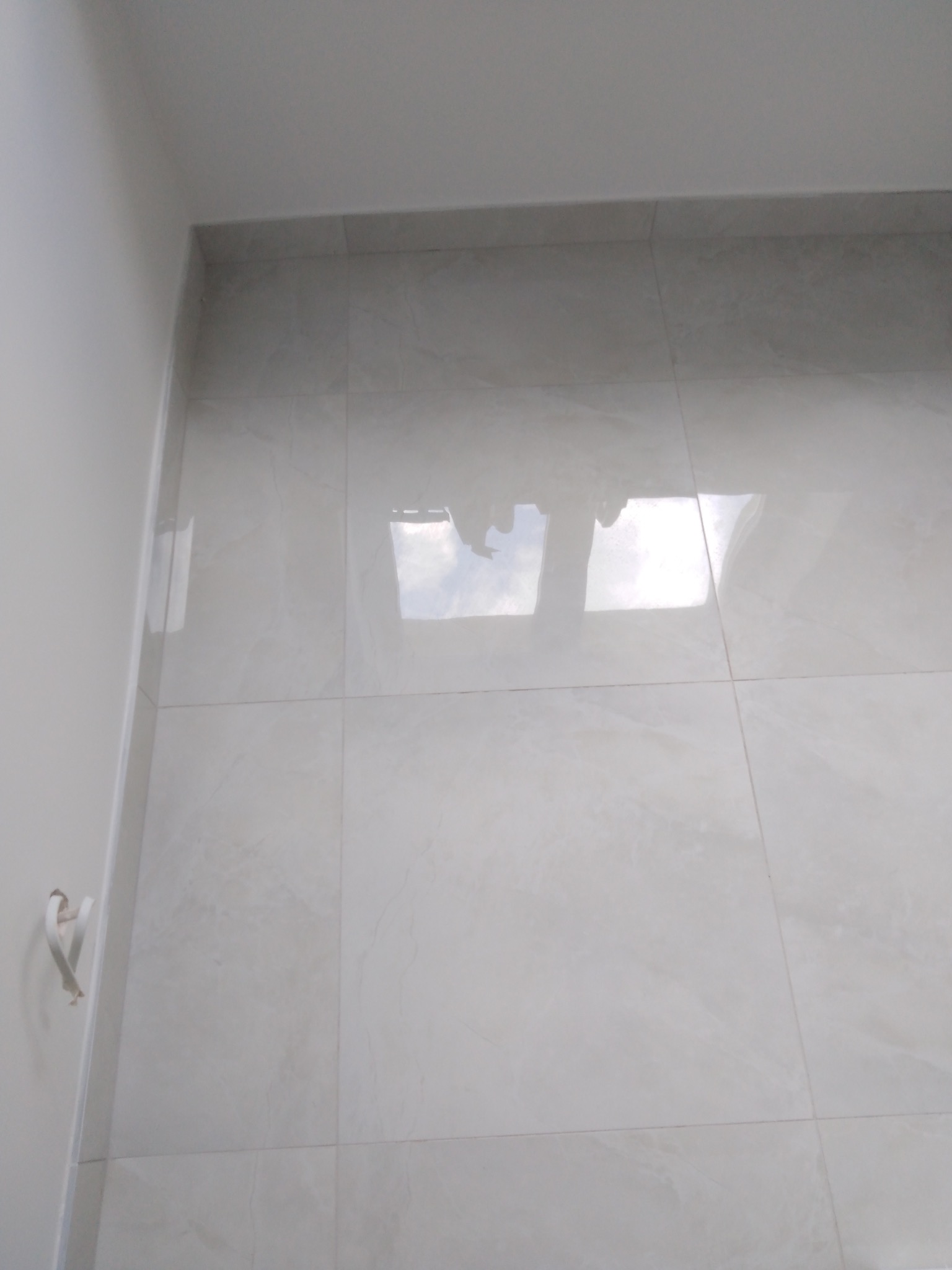 Błyszczące, jasne płytki ścienne z delikatnym wzorem marmuru, ułożone w regularny wzór. Widoczne odbicie światła na powierzchni płytek.