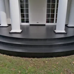 Elegancki taras z czarnych płytek kamiennych z trzema stopniami, otoczony białymi kolumnami i zielonym trawnikiem z opadłymi liśćmi.