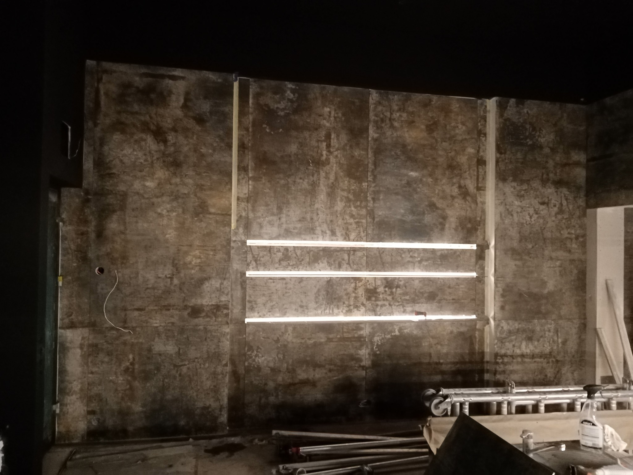 Montaż oświetlenia w pomieszczeniu z płytami imitującymi beton, widoczne przewody i rusztowanie