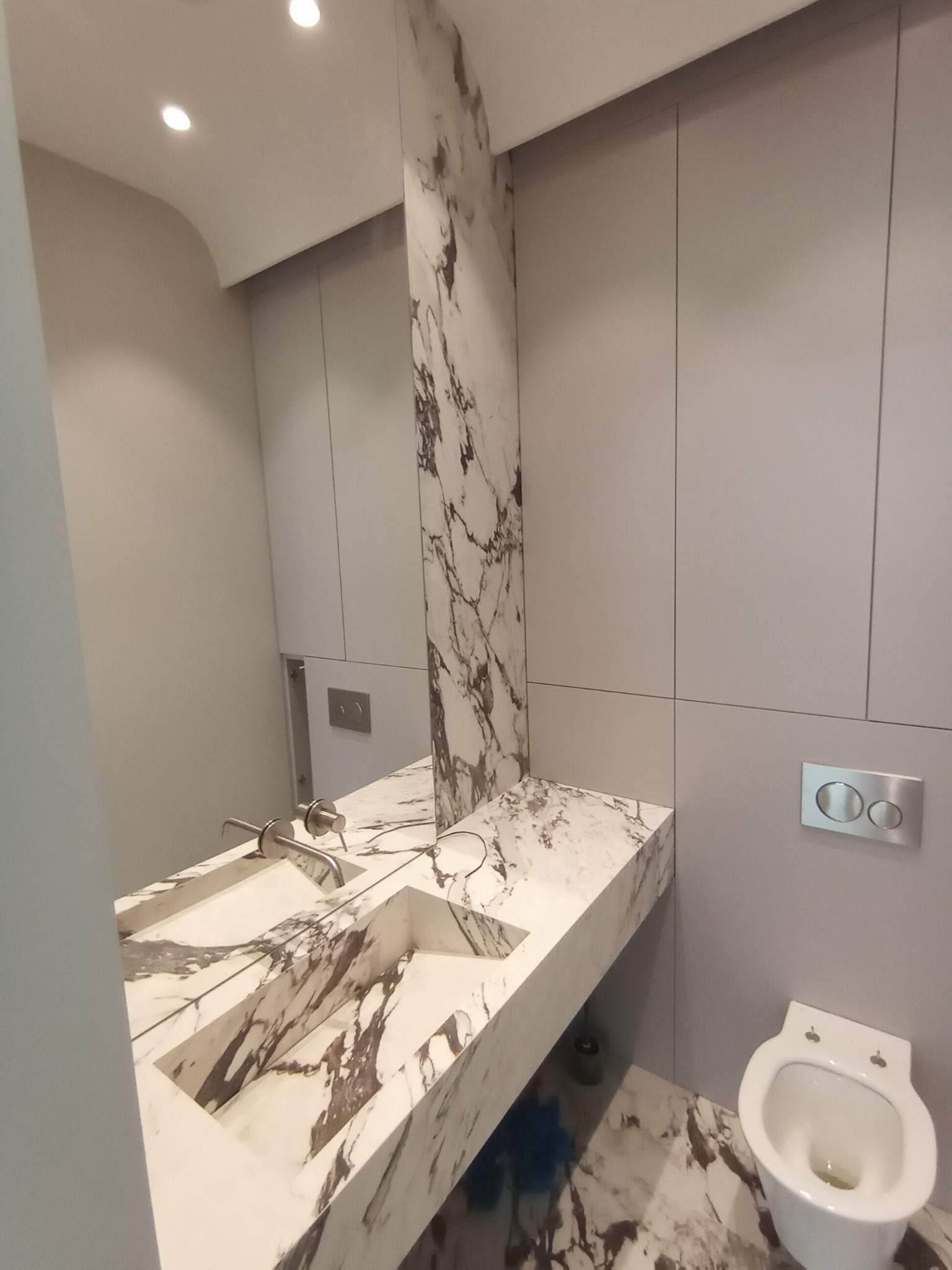 Nowoczesna łazienka z marmurową umywalką, blatem i podłogą w odcieniach bieli i szarości; minimalistyczne szafki i toaleta w tle.