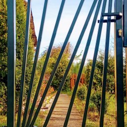 WAWRO - Nowoczesna brama wjazdowa z metalowymi, ukośnymi prętami, widziana z bliska na tle ścieżki w ogrodzie w Suchej Wielkiej.