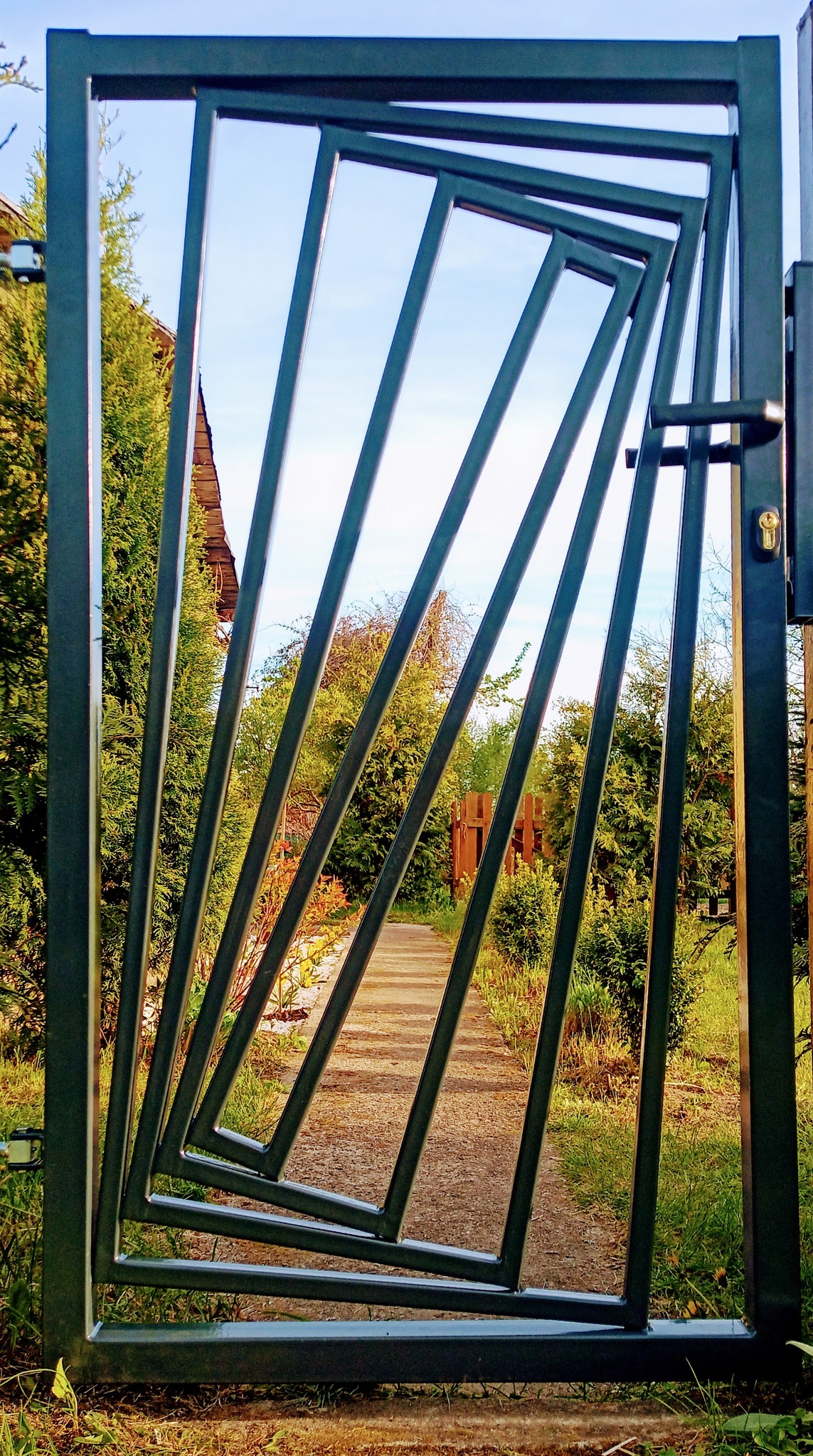 Nowoczesna brama wjazdowa z metalowymi, ukośnymi prętami, widziana z bliska na tle ścieżki w ogrodzie w Suchej Wielkiej.