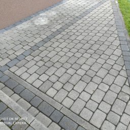 Stop Plamom - Ułożona kostka brukowa w odcieniach szarości, z obrzeżami i zieloną trawą w tle, tworząca estetyczny chodnik.