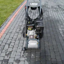 Profesjonalna myjka ciśnieniowa Lavor na kostce brukowej. Widoczne ślady wilgoci po myciu, sugerujące świeżo wykonaną usługę. Kadr z bliska, skupiony na urządzeniu.