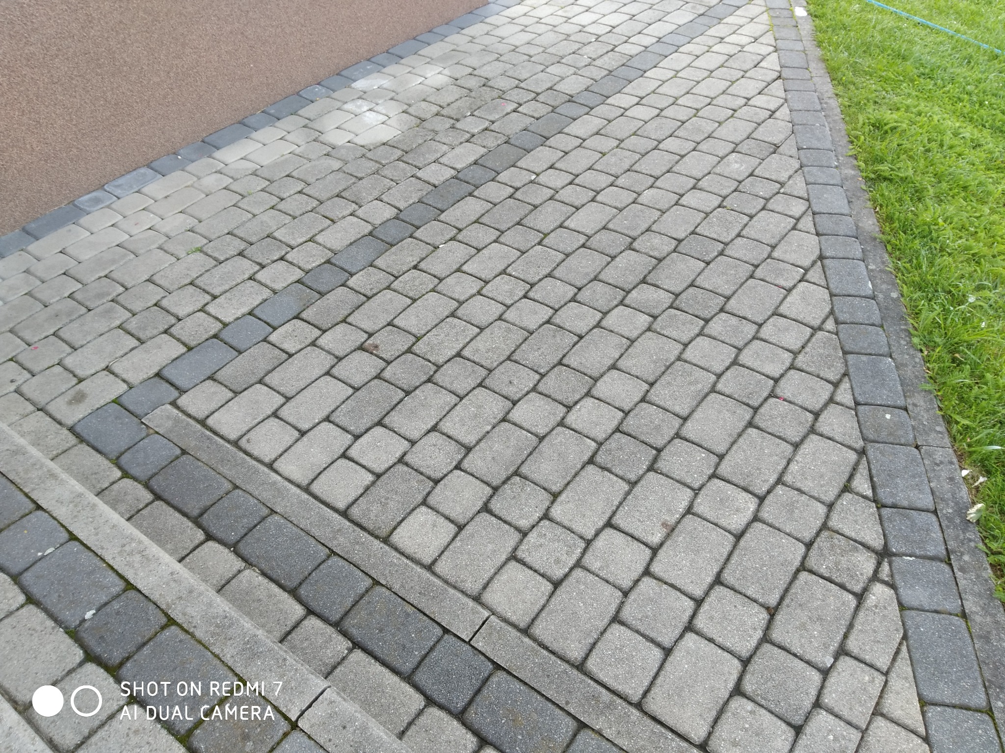 Ułożona kostka brukowa w odcieniach szarości, z obrzeżami i zieloną trawą w tle, tworząca estetyczny chodnik.