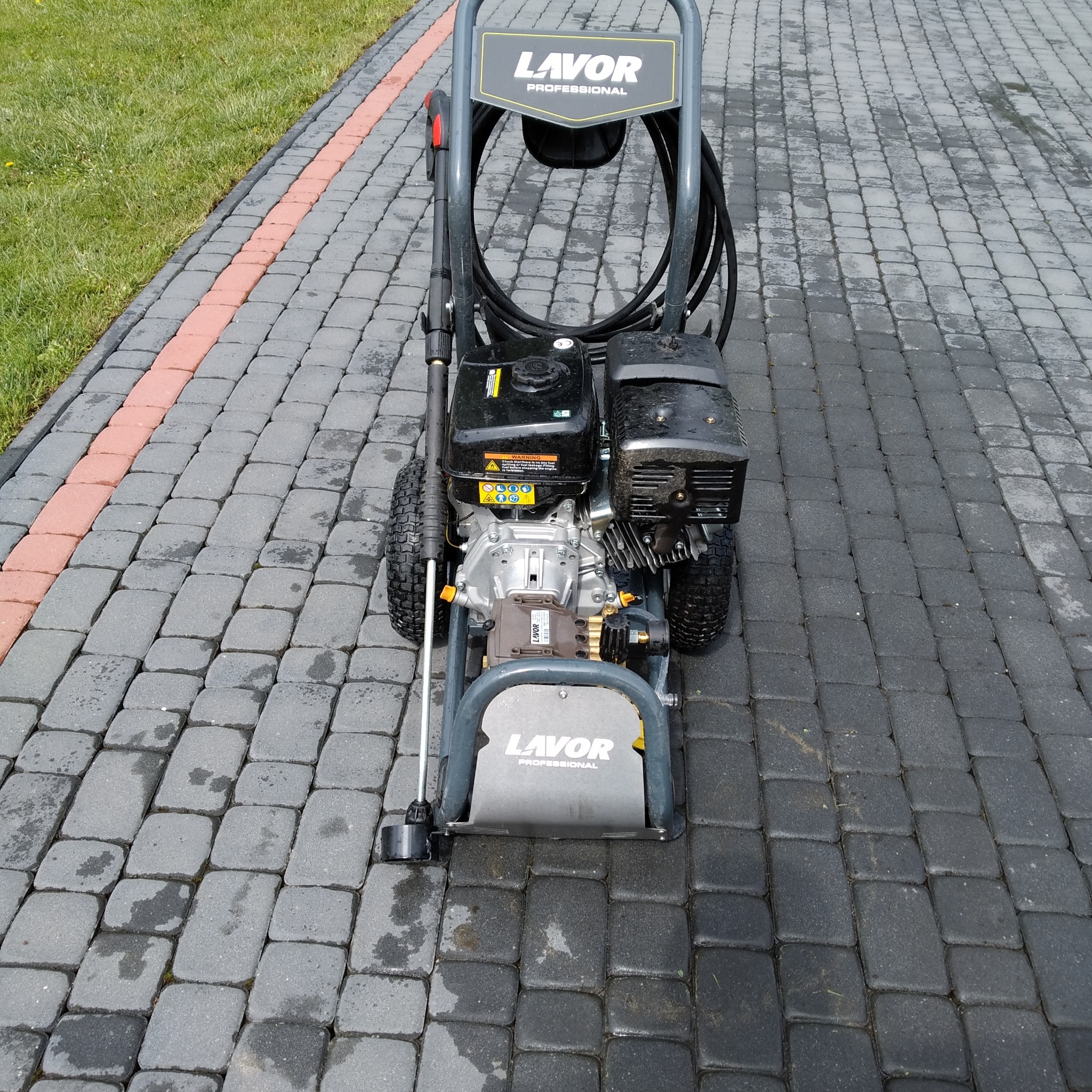 Profesjonalna myjka ciśnieniowa Lavor na kostce brukowej. Widoczne ślady wilgoci po myciu, sugerujące świeżo wykonaną usługę. Kadr z bliska, skupiony na urządzeniu.