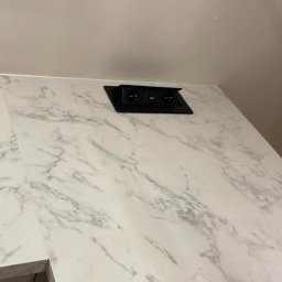 Pio-meb - Biały blat z efektem marmuru z wbudowanym, czarnym gniazdkiem elektrycznym.