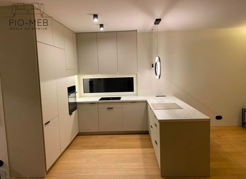 Jasna, minimalistyczna zabudowa kuchenna w Dobryszycach z blatem imitującym marmur, oświetlona nowoczesną, okrągłą lampą wiszącą.