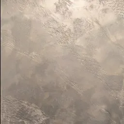 Ściana pokryta dekoracyjną, srebrzystą fakturą z wyraźnymi, poziomymi pociągnięciami, widoczne narzędzia malarskie w dolnej części kadru.