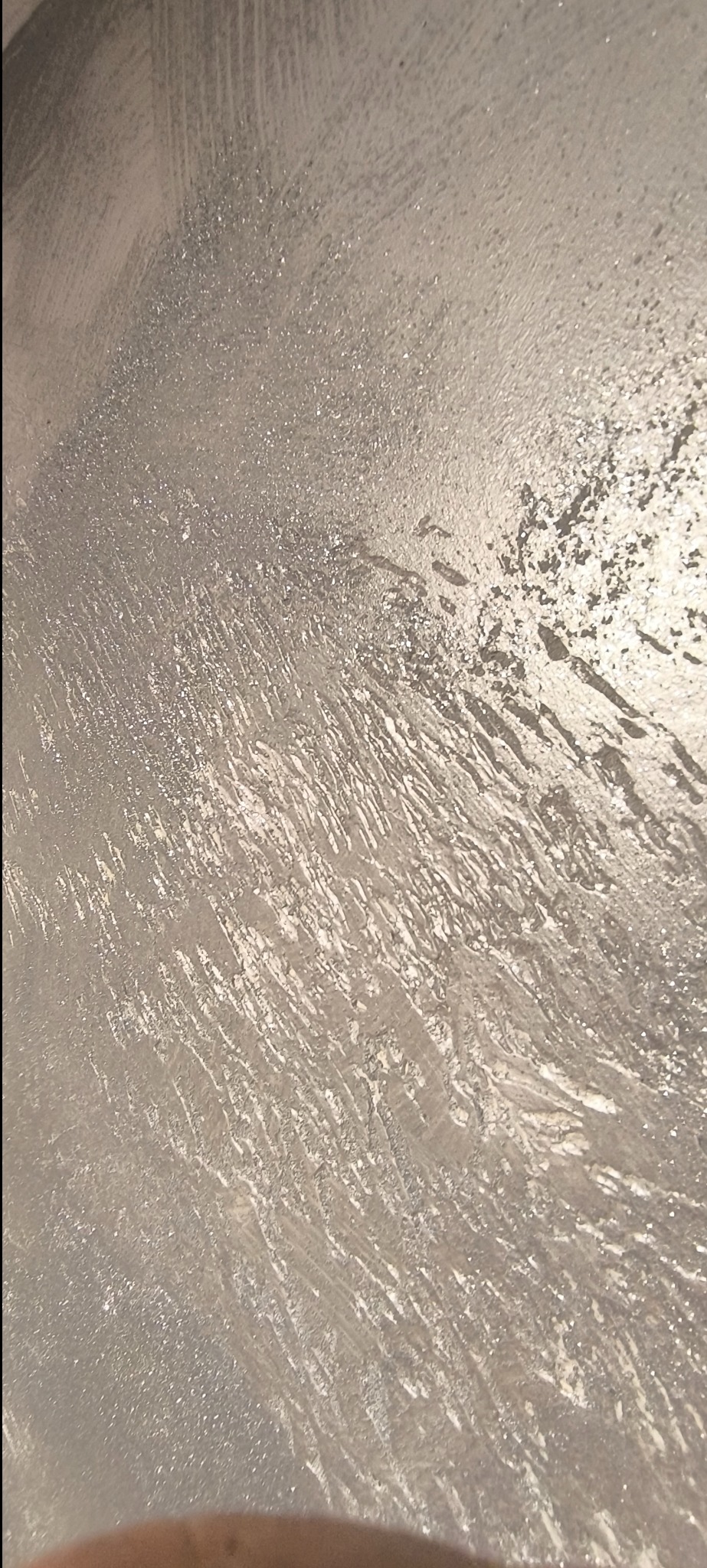 Ściana pokryta dekoracyjną srebrną farbą z wyraźnymi śladami pędzla, tworząca efekt tekstury i połysku.