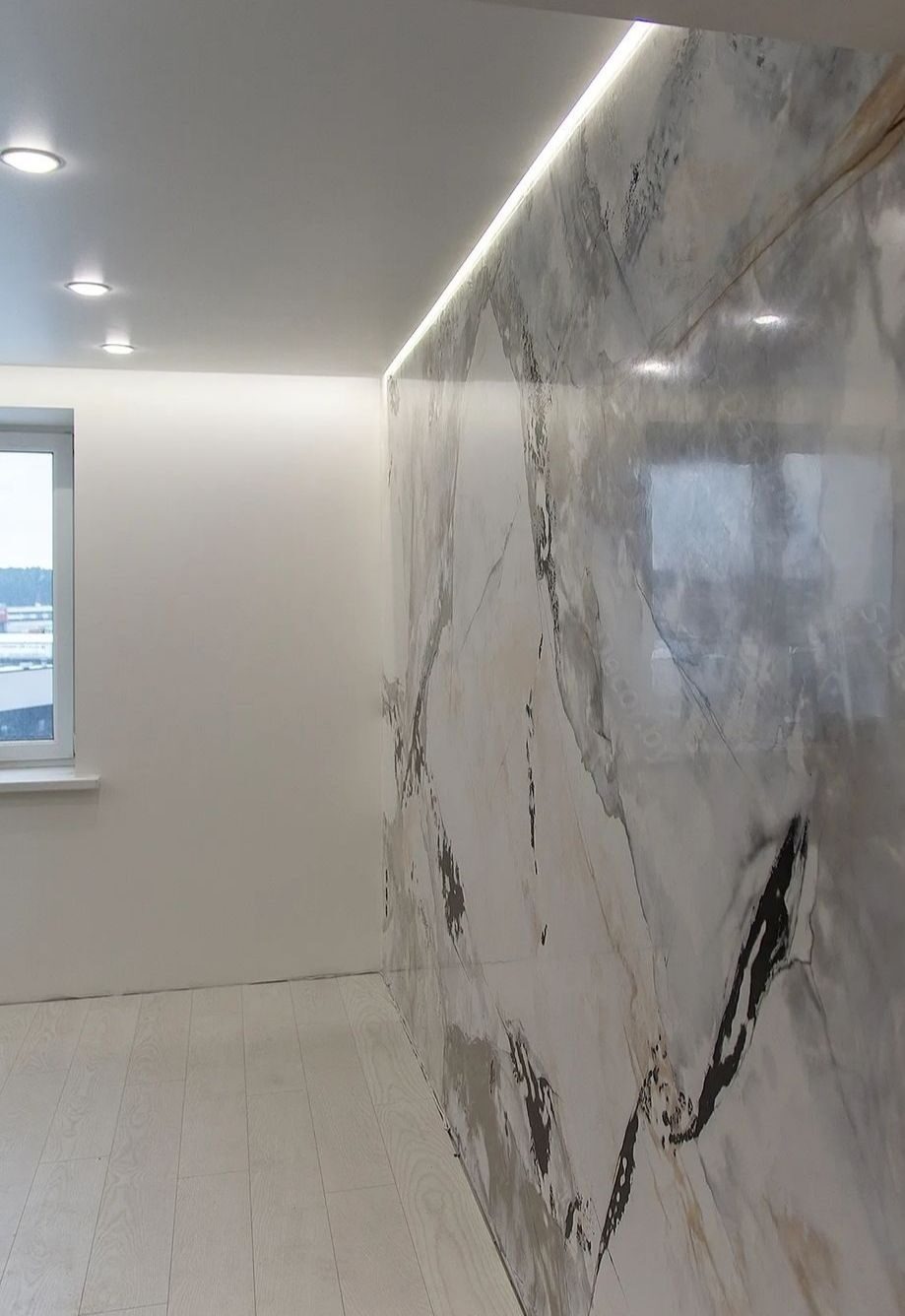 Ściana pokryta dekoracyjną gładzią imitującą marmur, z podświetleniem LED przy suficie, widoczne białe panele podłogowe i okno.