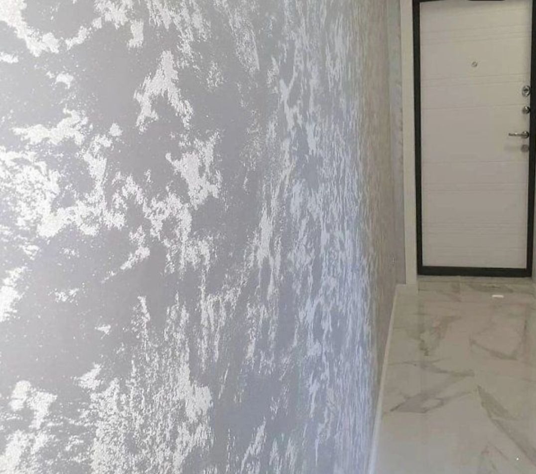 Ściana pokryta dekoracyjną gładzią w odcieniach szarości i bieli z efektem chmur, widoczna biała, nowoczesna drzwi z czarną ramą i marmurowa podłoga