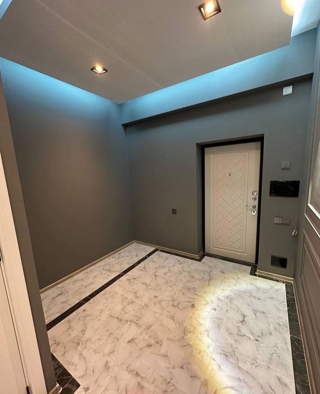 Wnętrze przedpokoju w Wasilkowie po remoncie: szare ściany, białe drzwi z geometrycznym wzorem, marmurowe płytki podłogowe z czarnym obramowaniem, oświetlenie punktowe w suficie.