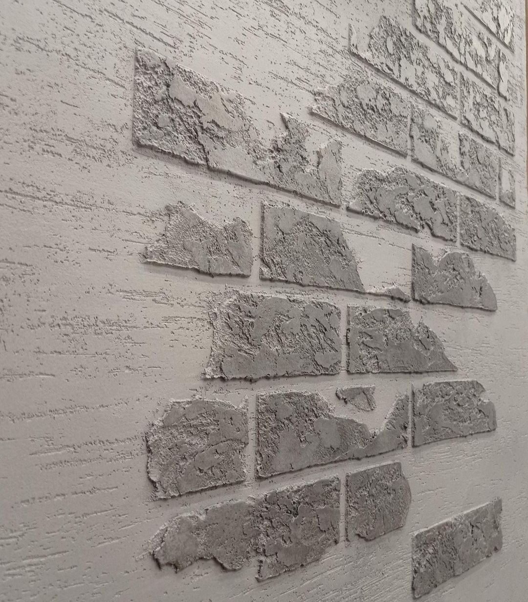 Dekoracyjna ściana z efektem cegły w odcieniach szarości, wykonana z fakturą imitującą surowy kamień, z widocznymi nierównościami i chropowatościami.