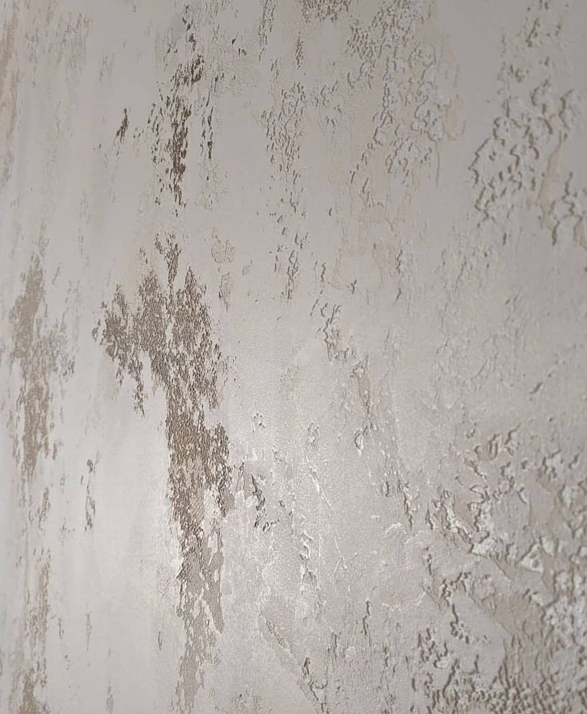 Ściana pokryta dekoracyjną, strukturalną powłoką w odcieniach szarości i bieli, z wyraźnymi nieregularnościami i fakturą imitującą naturalny kamień lub tynk.