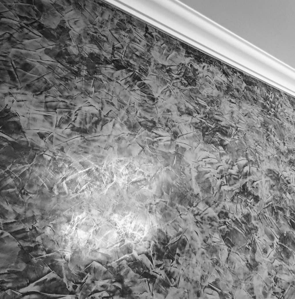 Czarno-białe zdjęcie ściany z dekoracyjną strukturą gładzi, widoczna listwa przysufitowa.