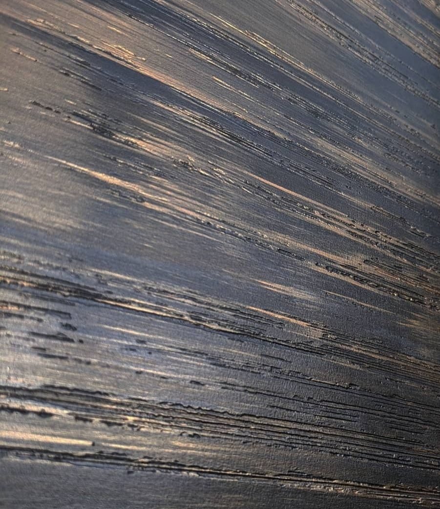 Ściana z ciemną, strukturalną farbą, z widocznymi śladami pędzla tworzącymi prążkowany wzór. Tekstura przypomina surowe drewno lub efekt postarzenia.